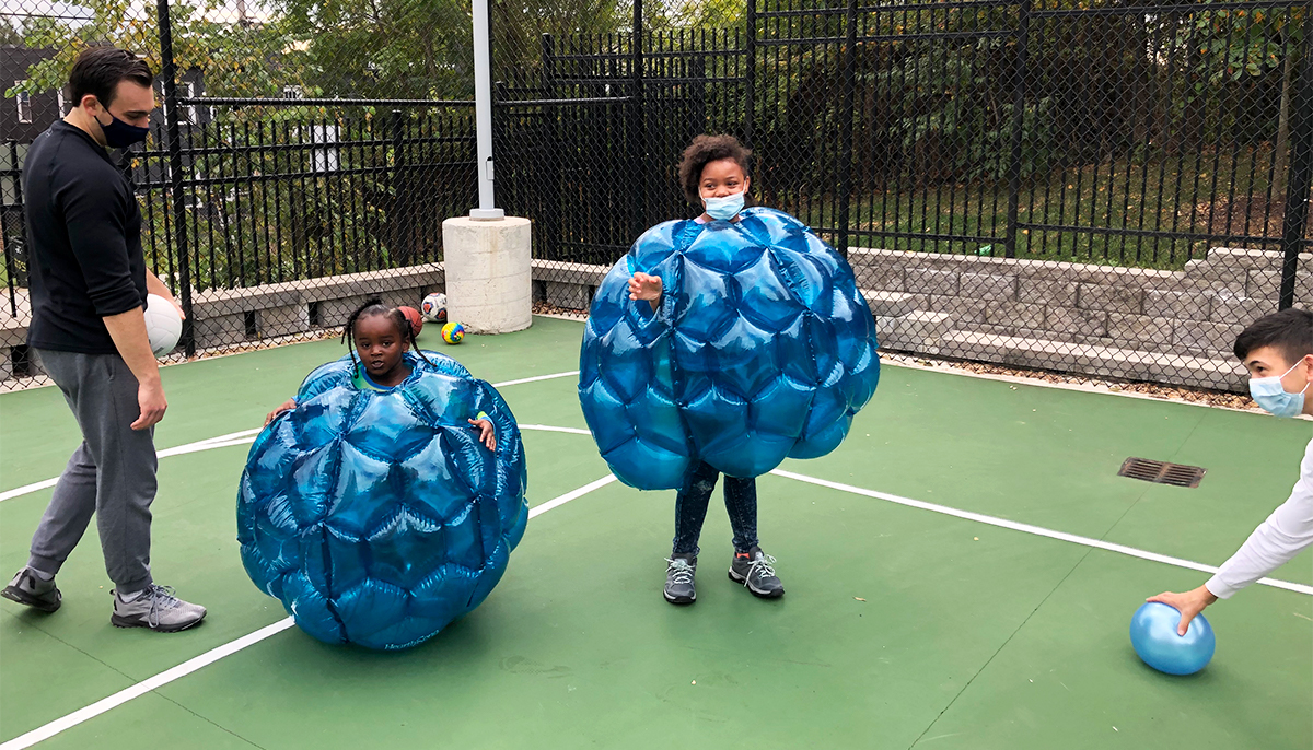 Two students assist two children who are wearing inflatable bumper balls