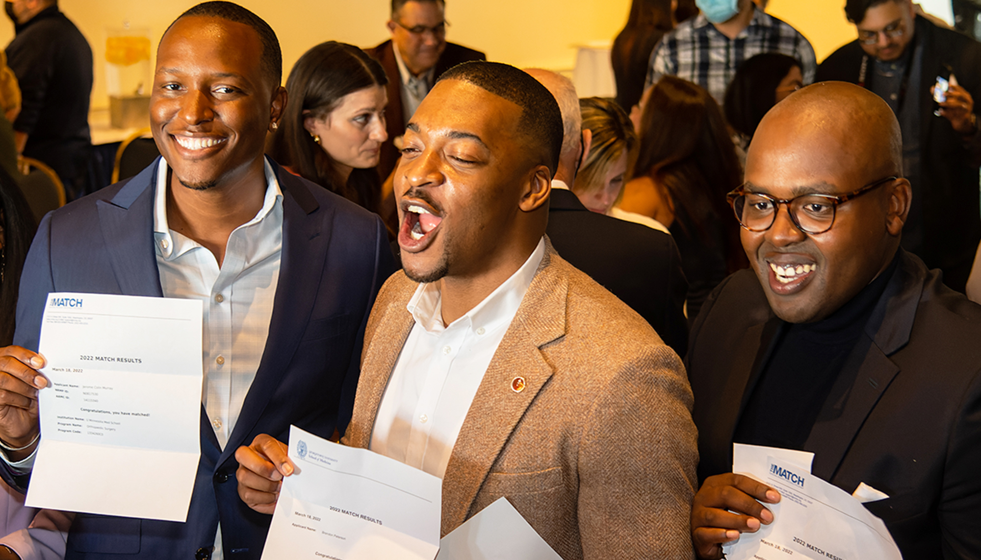 Three men smile and hold their Match Day letters during this year's ceremony