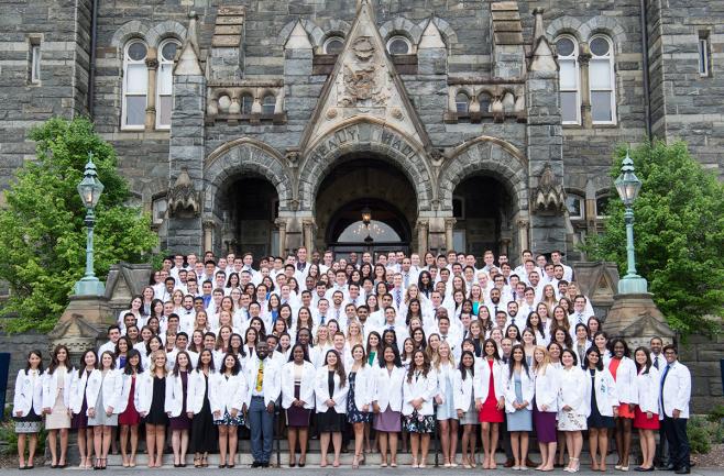 Students in the class of 2022 stand on the steps in front of Healy Hall wearing their short white coats