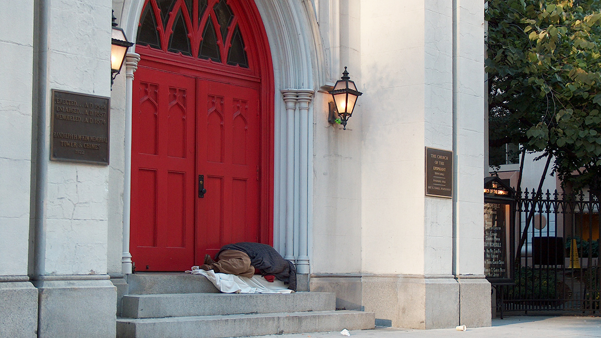 A person wrapped in blankets who may be experiencing homelessness sleeps in the doorway of a church