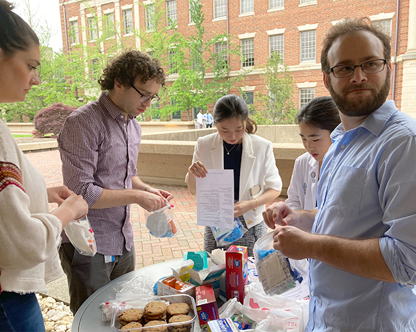 A group of five people stand around a table putting first aid items into plastic zip-top bags.