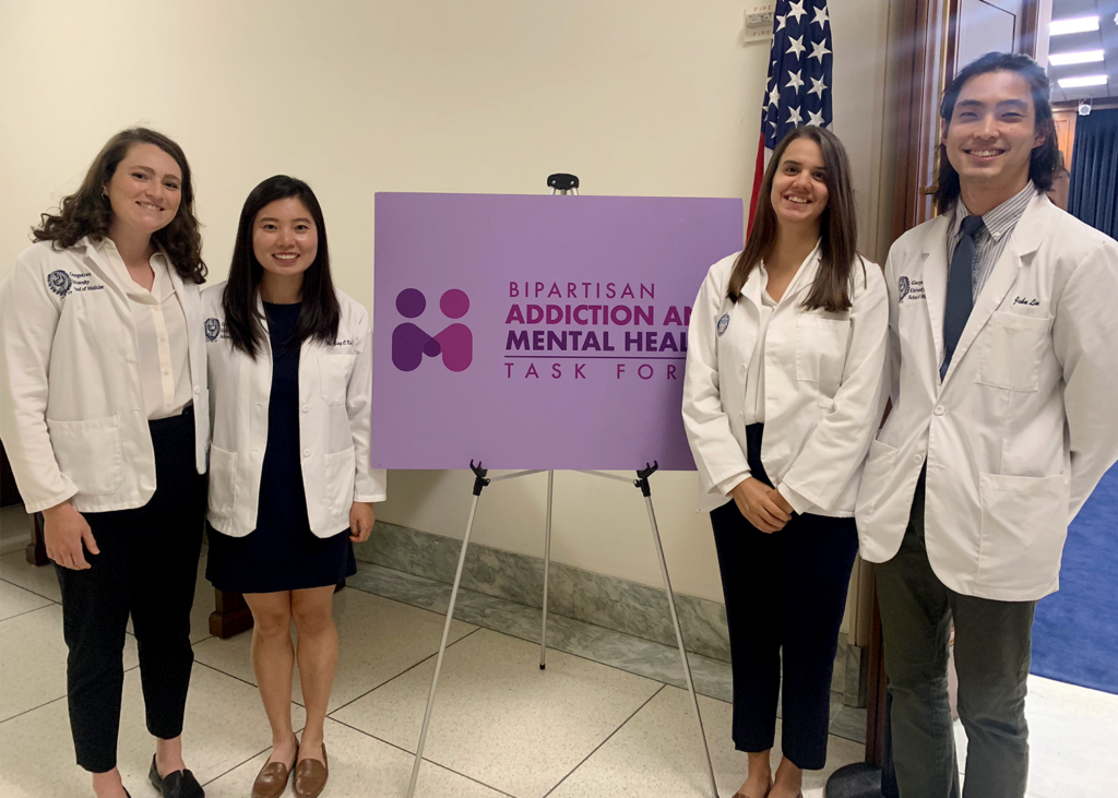 Four students stand together with a sign that reads Bipartisan Addiction and Mental Health Task Force