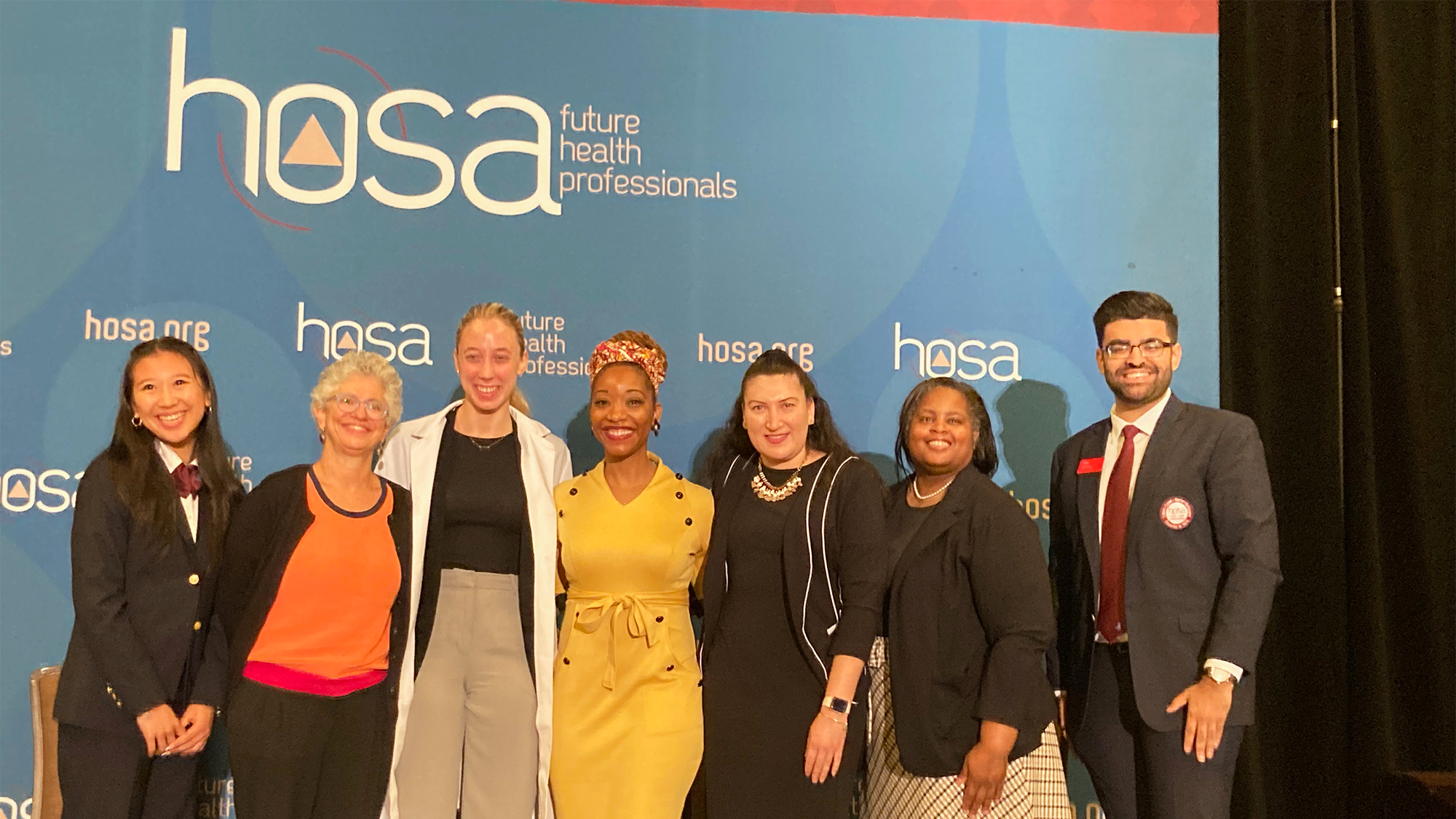 A group of people stand before a backdrop with the HOSA logo