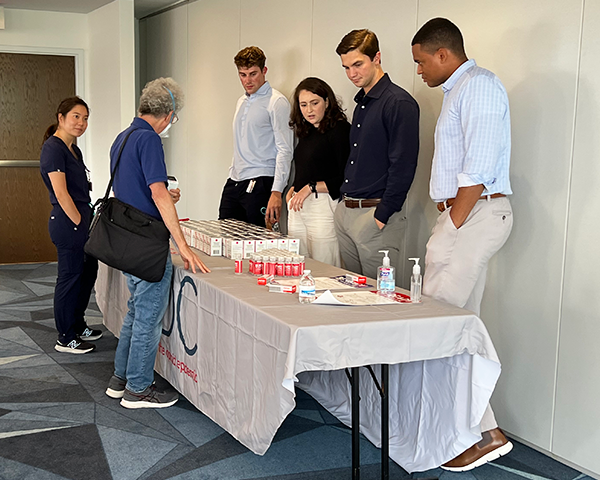 Several people stand around a table lined with boxes of Narcan for distribution