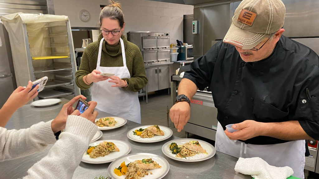 Chef Molina puts the finishing touches on a dish, while students take pictures of the plated food with their phones