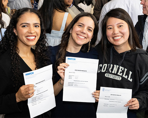 Three medical students hold their letters up for the camera and smile