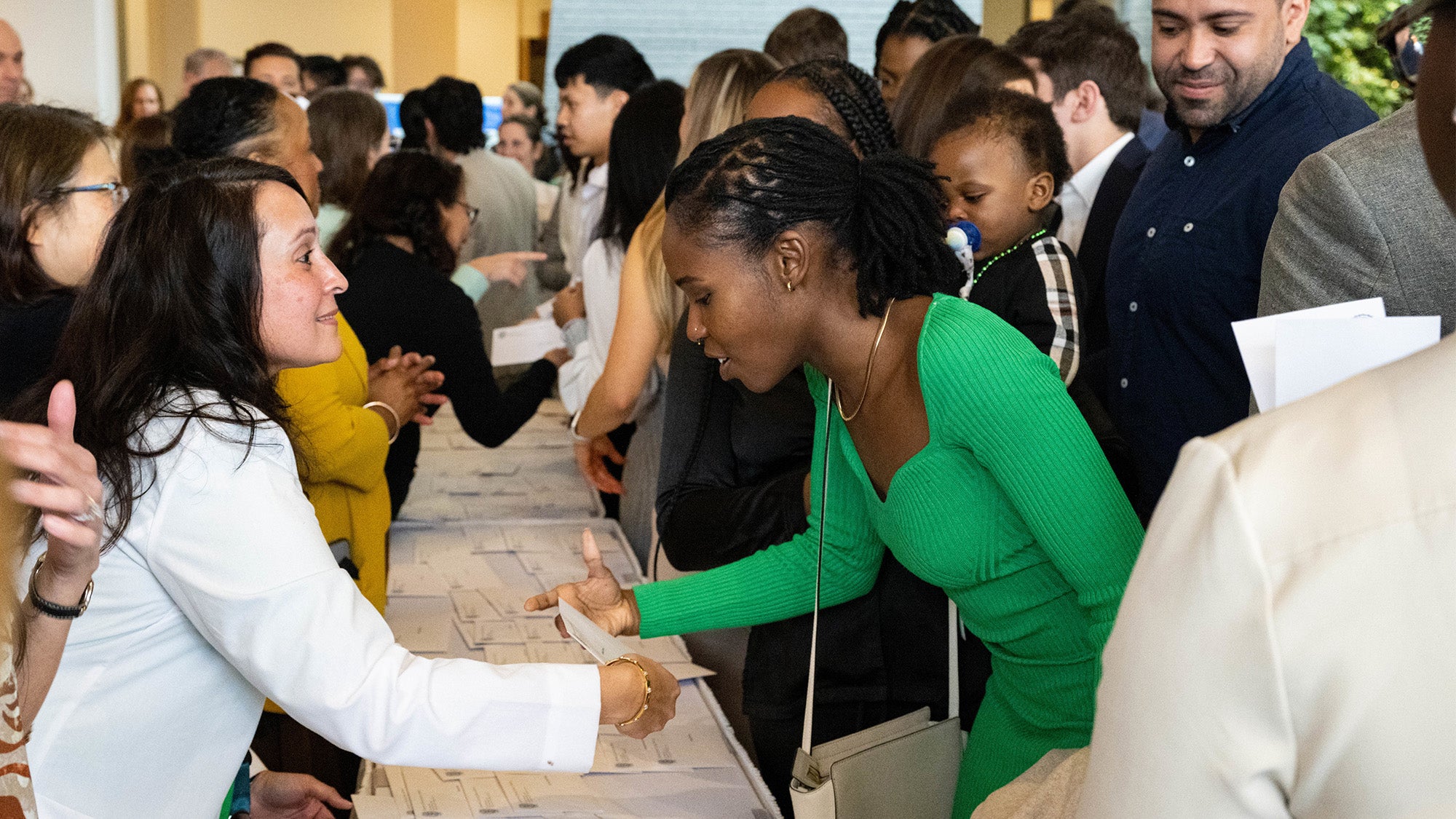 A faculty member hands a medical student her letter across a table filled with similar letters