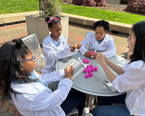 A group of three young students work with a medical student to answer questions