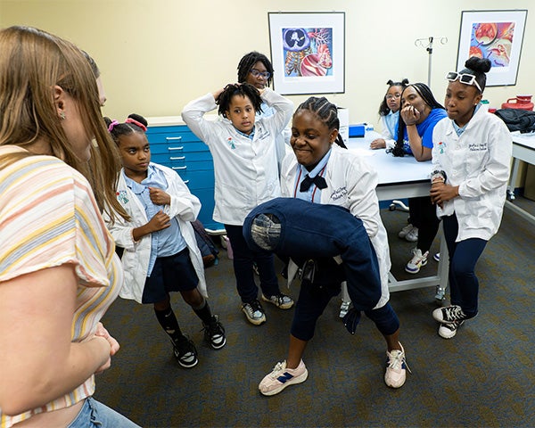 A young student squeezes a dummy while other students and the instructor look on