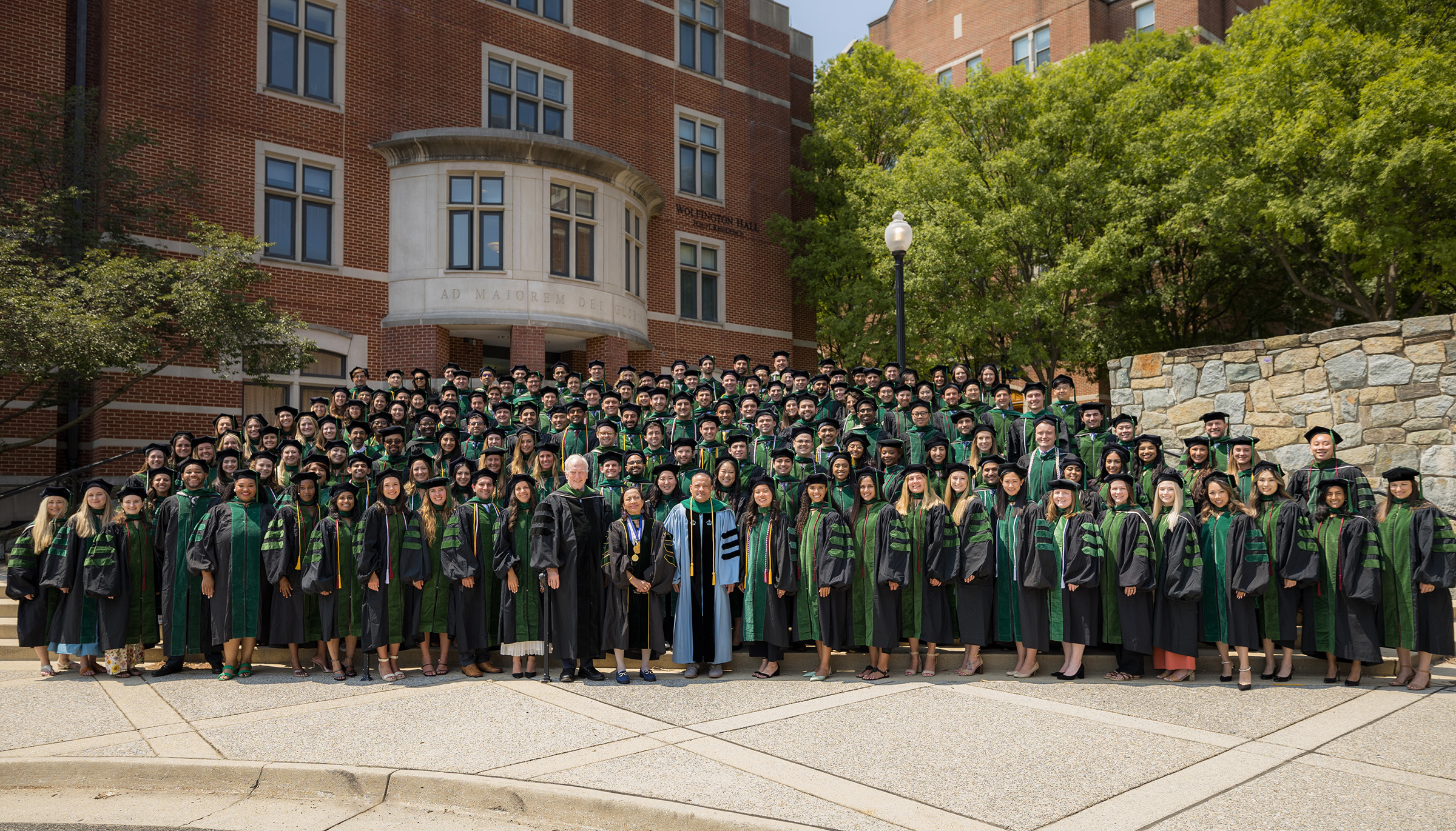 The 200 members of the graduating class of 2023 stand together dressed in academic regalia on the steps outside Wolfington Hall on campus