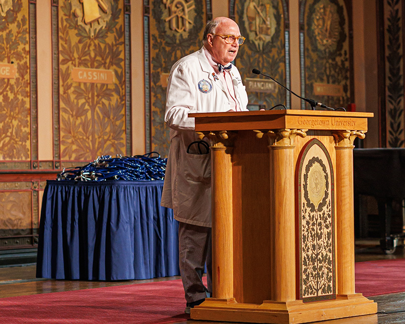 Dr. Mitchell speaks from a podium onstage in Gaston Hall