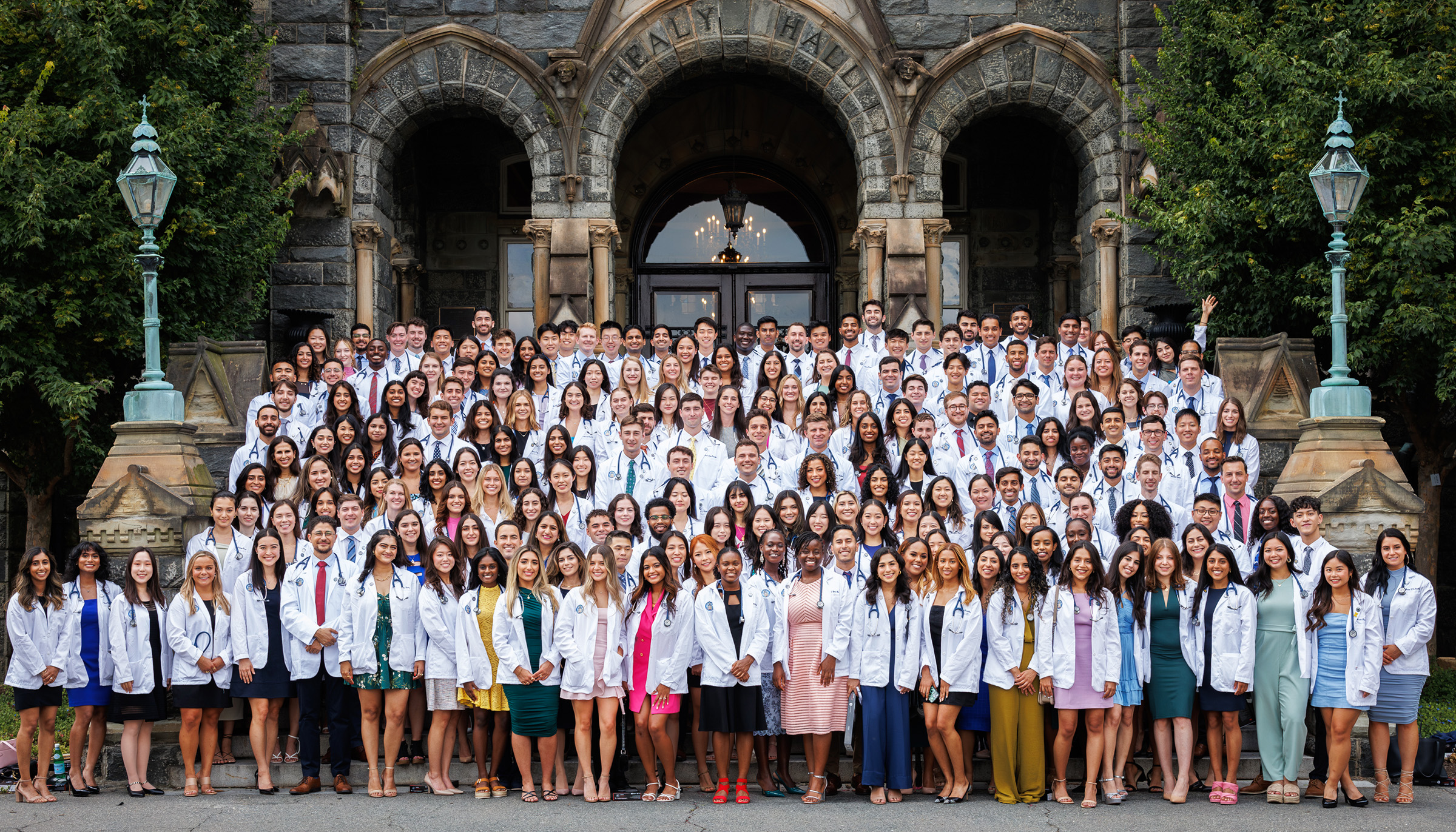 The Class of 2027 stands as a group in their white coats on the steps of Healy Hall