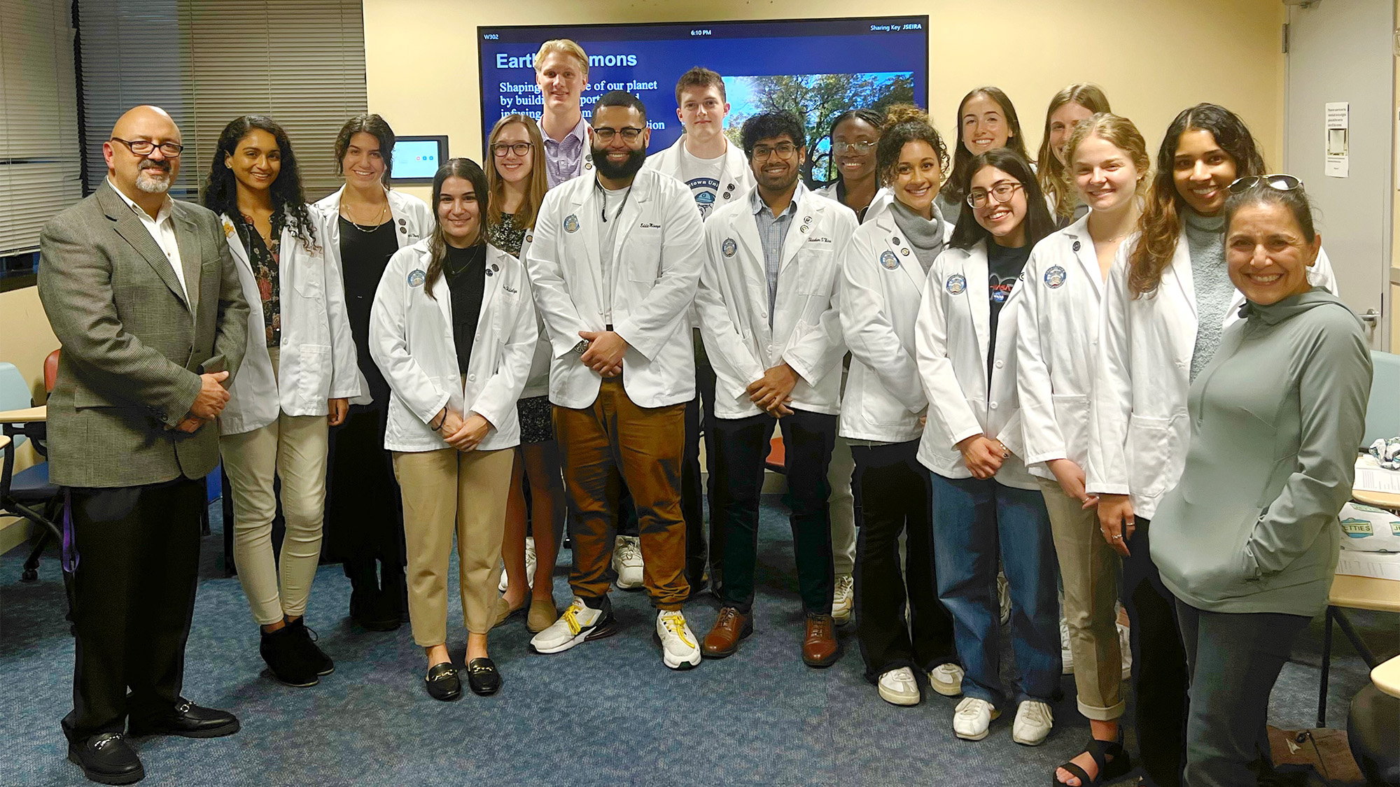 A group of students in white coats comprising the Medical Spanish Initiative stand with their faculty advisors as a group