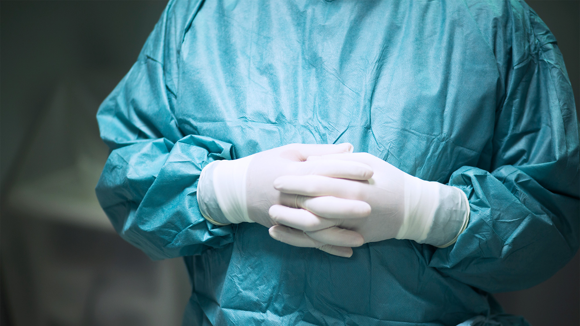 A person in surgical garb folds their gloved hands