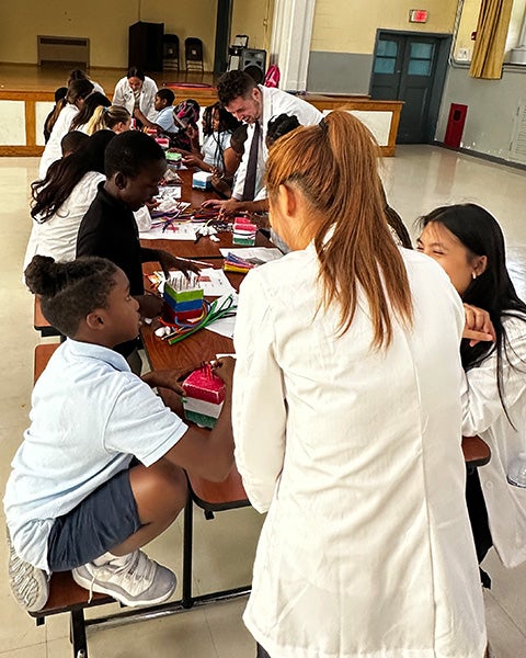 Students sit at a table doing an activity while medical students help them