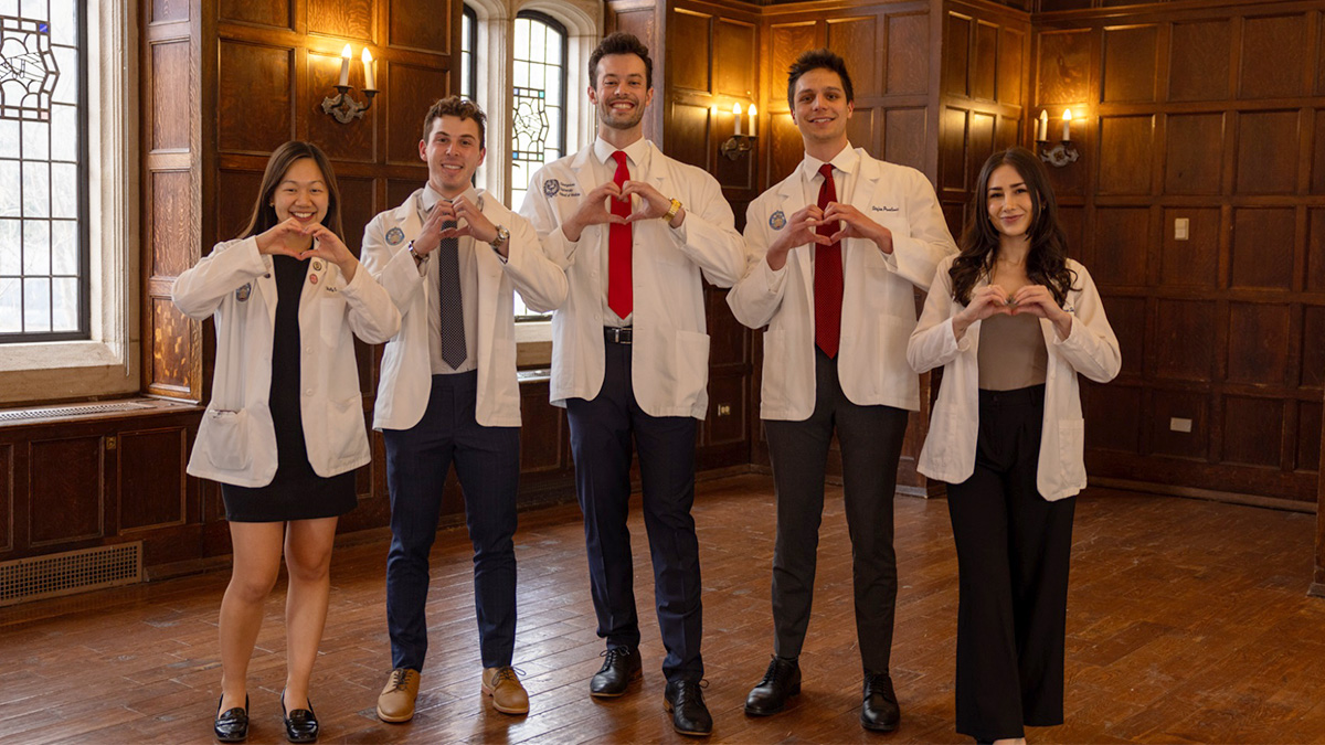 Five medical students stand together holding their hands in the shape of hearts