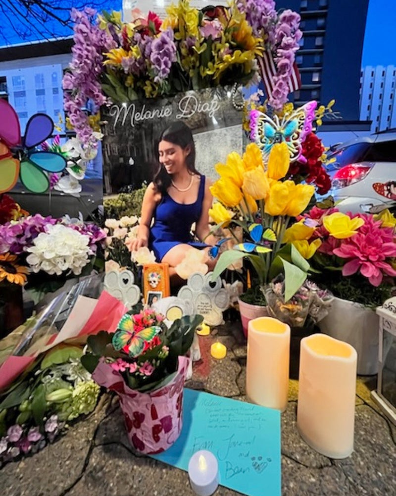 A large collection of memorial items including candles, flowers and cards clusters around a poster of Diaz attached to a light pole on a street