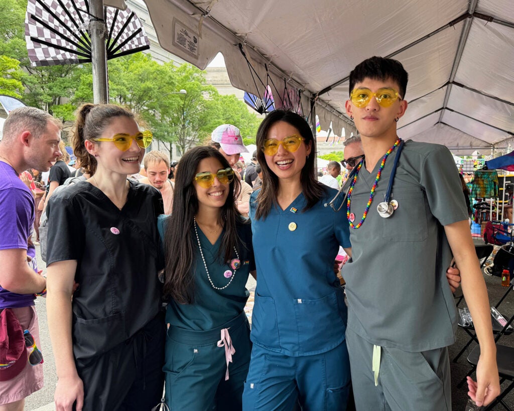 Four students stand side by side wearing scrubs and yellow plastic novelty glasses