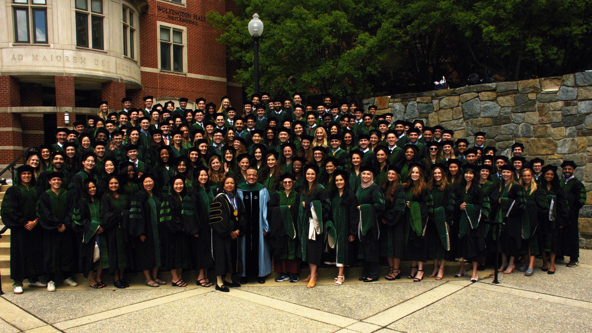 The class of 2024 stands together as a group dressed in academic regalia outside Wolfington Hall on campus