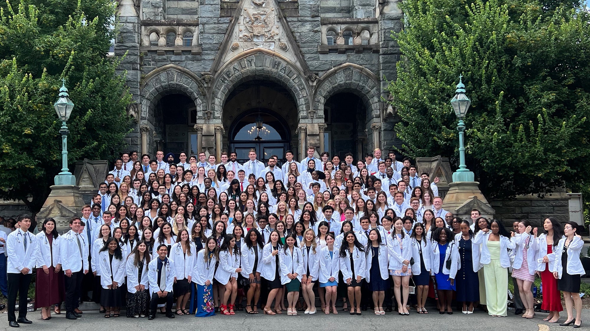 The members of the class of 2028 stand together on the steps of Healy Hall with their new white coats on