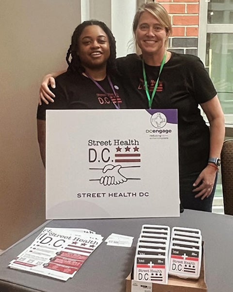 Tobie Smith and fellow worker stand together behind a table featuring Street Health DC marketing materials