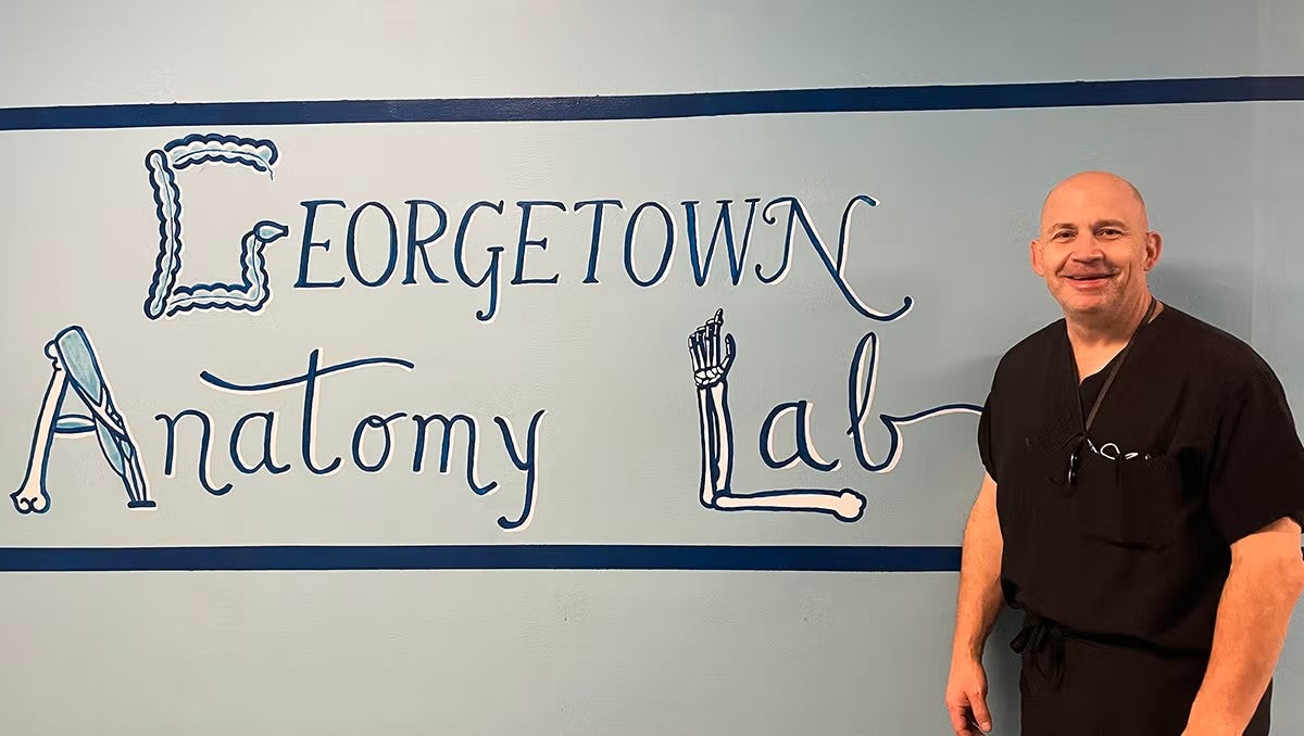 Marc Zavoyna stands in front of a mural with the words Georgetown Anatomy Lab spelled out in script and illustrations of human bones