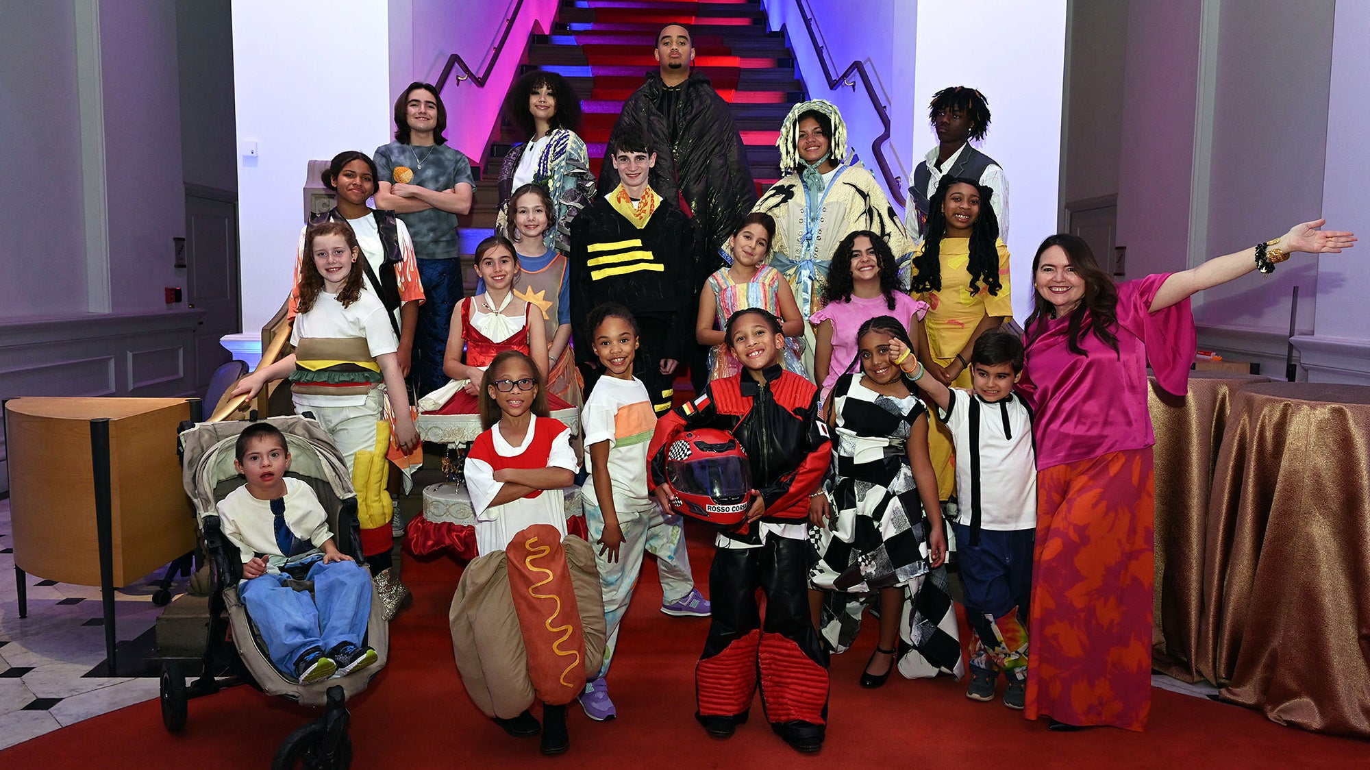 Children and youth of various genders and races stand together each wearing creative and whimsical fashion designs, Dr. Serrano stands with them