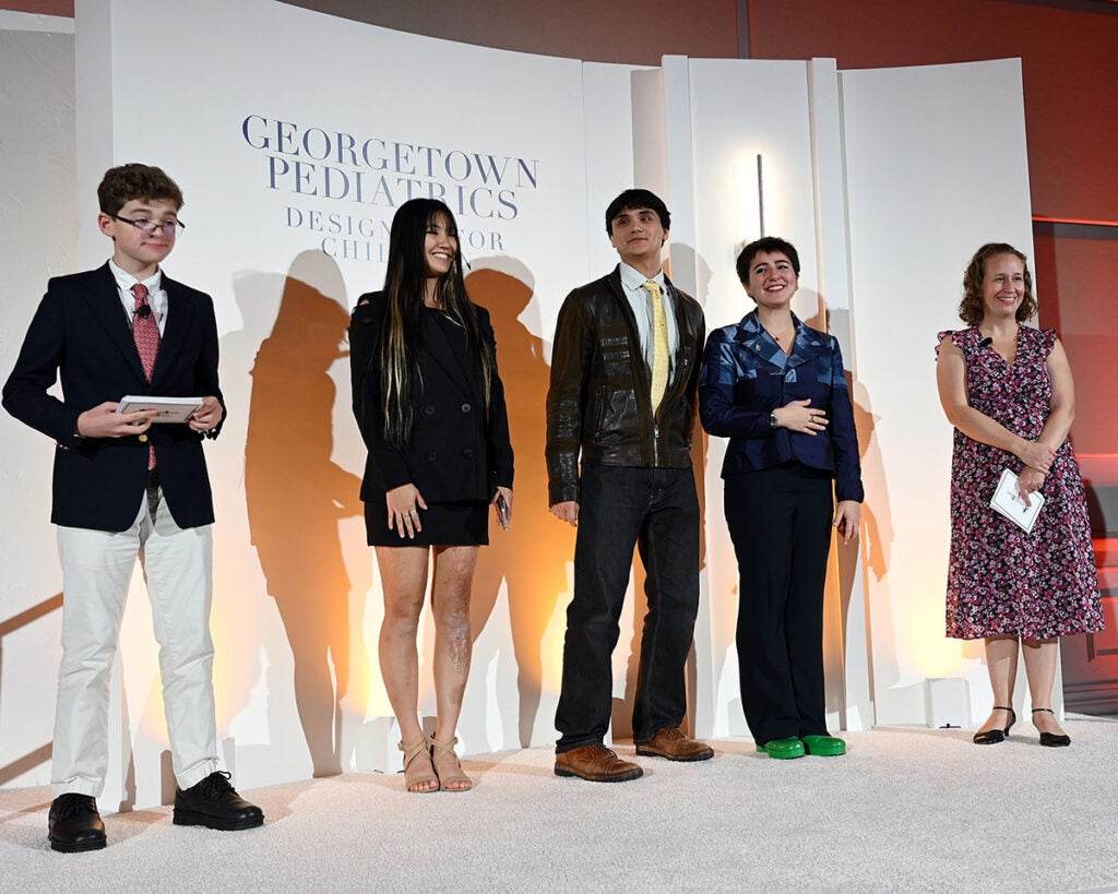 Three of the young adult designers stand onstage with the two event emcees on either side of them