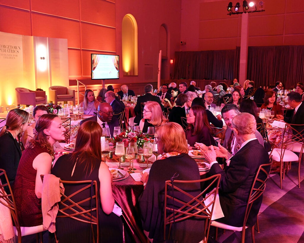 A view of the Renwick Gallery space filled with tables at which gala attendees sit eating their meals and talking