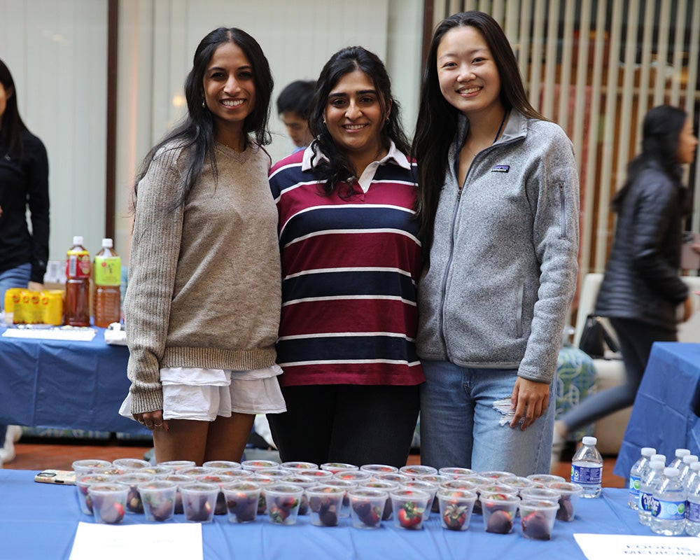 Three students stand together behind a table set with chocolate covered strawberries in plastic cups