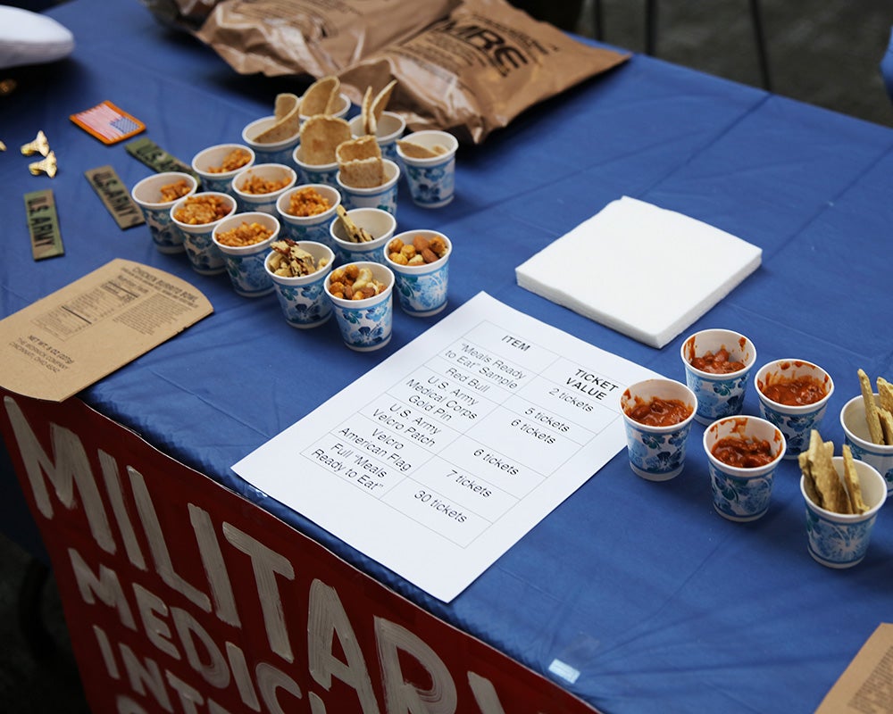 Samples of MREs sit in rows on a table with a sign and additional items for purchase