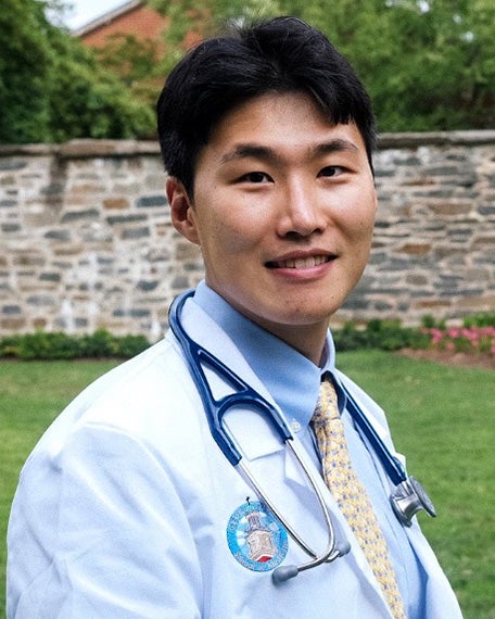 Jason Lim in white coat with stethoscope on campus
